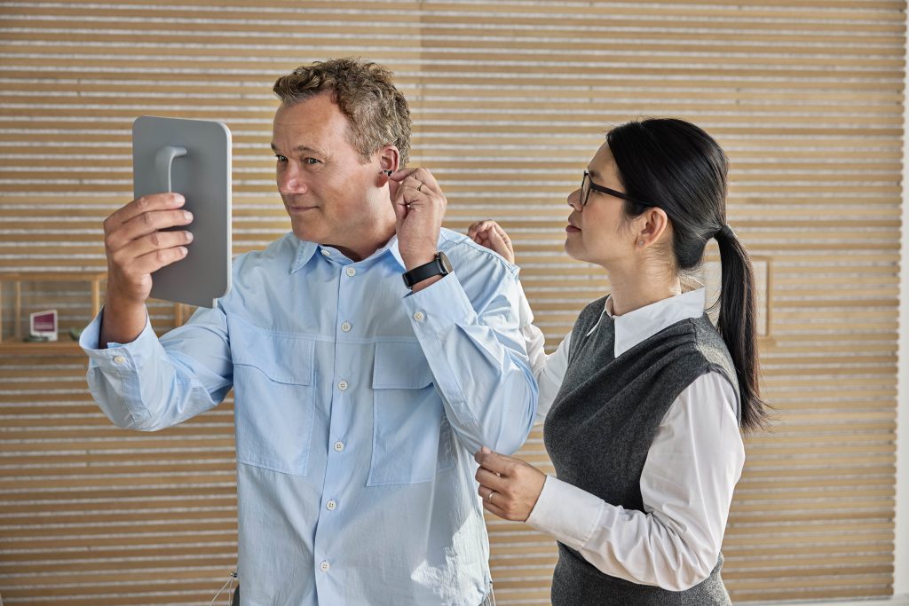 Audiologist fitting a custom Oticon hearing aid for a patient